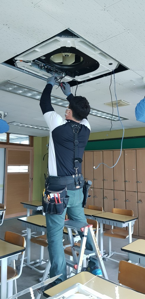 학교 교실에서 천장형 에어컨을 청소하는 작업자